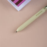 Light green pen on a beige surface with a pink and white striped object in the background