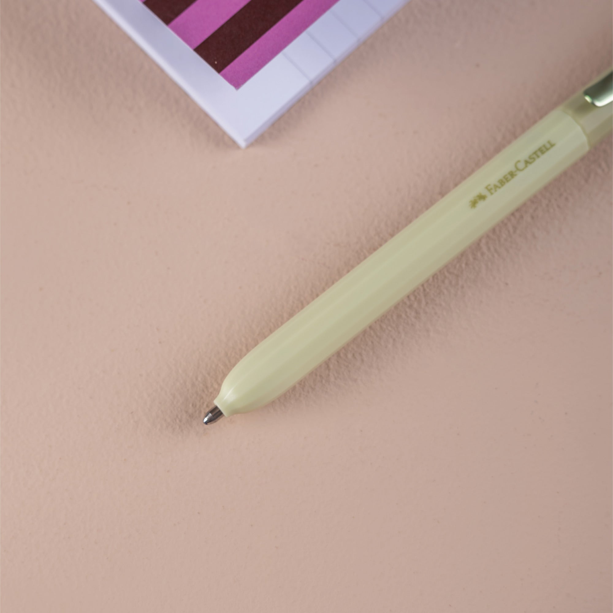 Light green pen on a beige surface with a pink and white striped object in the background