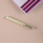 Green pen on a pink surface with a striped notebook in the background