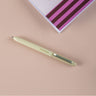 Green pen on a pink surface with a striped notebook in the background