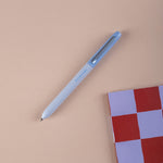 Light blue ballpoint pen on a beige surface with a checkered notebook