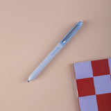 Light blue ballpoint pen on a beige surface with a checkered notebook