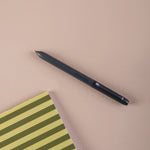 Black ball point pen on a beige surface with a green and yellow striped notebook