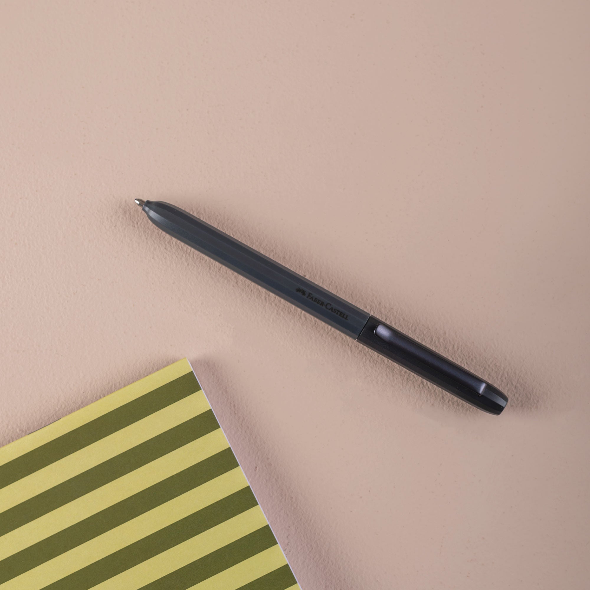 Black ball point pen on a beige surface with a green and yellow striped notebook