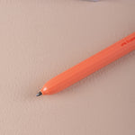 Orange ball point pen on a beige surface