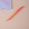 Orange ball point pen on a beige surface with a purple notepad in the corner.