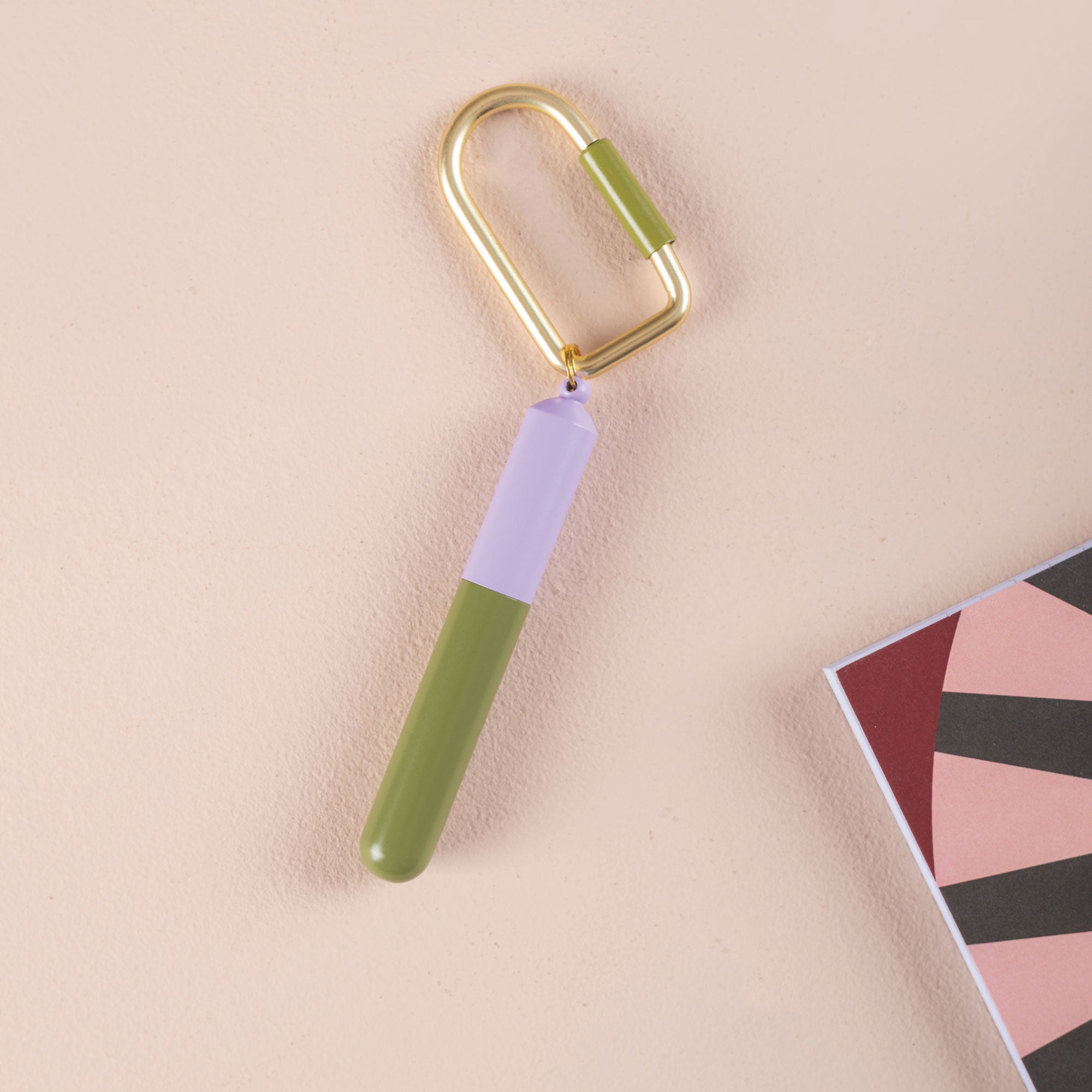Mini pen on a gold key chain in colours  Purple and Green on a beige background