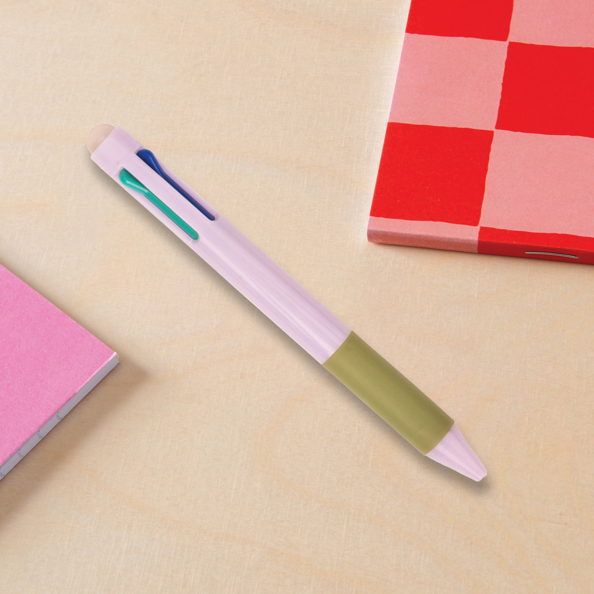 Multicolored pink pen on a beige surface with a red checkered notebook in the background.