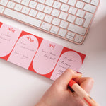 Hand writing on a red planner with a keyboard in the background