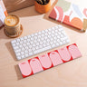 Keyboard on a desk with a pink and red weekly planner pad. 