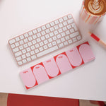 Pink keyboard and mouse pad on a white surface with a coffee cup and pen.