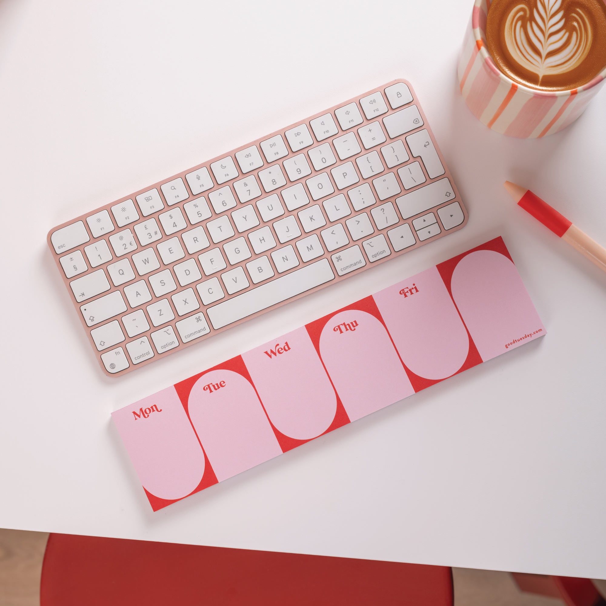 Pink keyboard and mouse pad on a white surface with a coffee cup and pen.