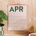 2025–2026 Simply Bright A4 Wall Calendar displayed on a wall above a desk, illustrating its practical use in a workspace setting
